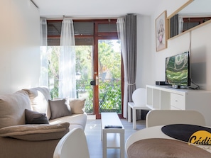 A modern living room with a sofa, a coffee table, a TV, and a balcony with curtains. - Apartamento Plaza Mina by Cadiz Time (Cádiz)