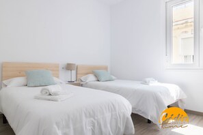Two single beds with white bedding and light blue pillows, a wooden headboard, a nightstand with a lamp, and a window with a view of buildings. - Casa del Fotografo by Cadiz Time (Cádiz)