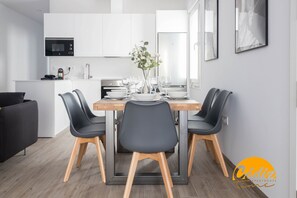 A modern kitchen with white cabinets, a microwave, and a dining table set for four with black chairs. - Casa del Fotografo by Cadiz Time (Cádiz)