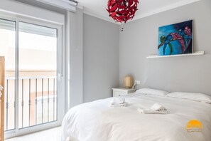A hotel room with a bed, a painting, a nightstand, a lamp, and a view of the outside balcony. - Casa Arcoiris by Cadiz Time (Cádiz)