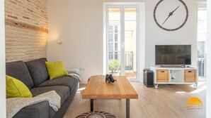 Una sala de estar moderna con un sofá gris, una mesa de centro de madera, un televisor sobre un soporte blanco y una pared de ladrillo.