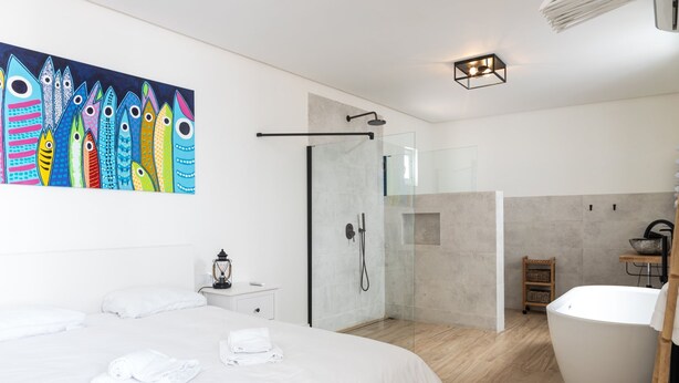 Una habitación de hotel moderna con una cama grande, un box de ducha con paredes de vidrio, una bañera y un cuadro de peces de colores en la pared.