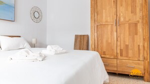 Ett hotellrum med en säng, vita sängkläder, en garderob i trä, ett konstverk på väggen och en flätad korg.