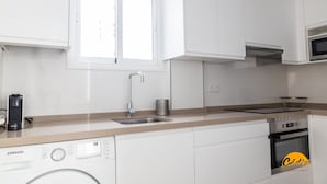 Ett modernt kök med vita skåp, en diskho i rostfritt stål, en inbyggd mikrovågsugn och en diskmaskin från Samsung.