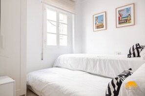 Ein Schlafzimmer mit zwei Betten, einem Fenster und zwei gerahmten Bildern an der Wand.