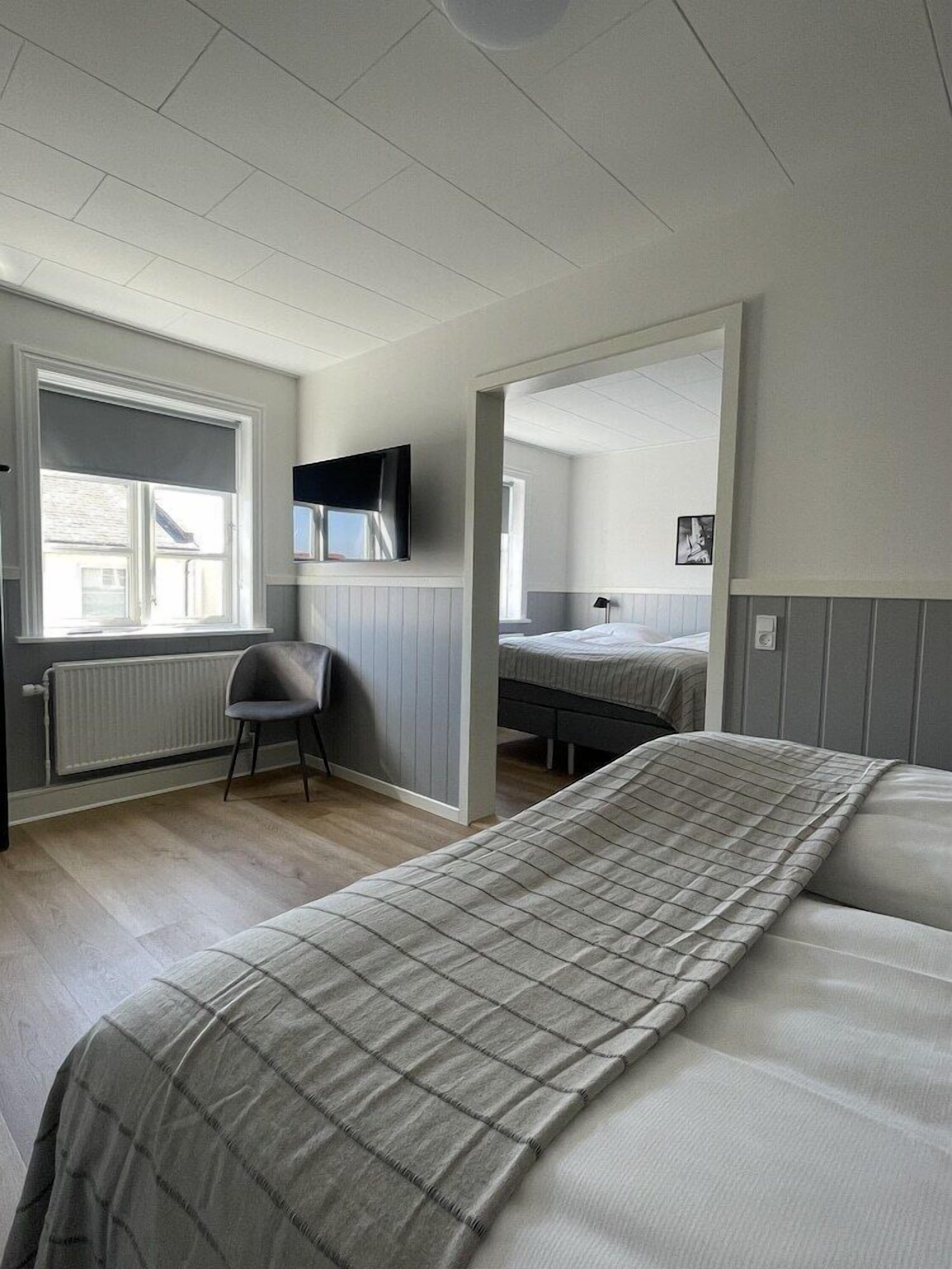 A bedroom with a bed, a chair, a TV mounted on the wall, and a window with a view of the outside.