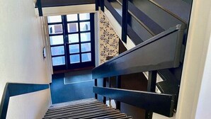 Μια σκάλα με μαύρα κάγκελα και ένα διακοσμητικό χαλί. Πάνω από τη σκάλα υπάρχουν πινακίδες που υποδεικνύουν τους αριθμούς δωματίων 7-37 και 2-6.
