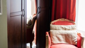Ein Zimmer mit einem Holfachschrank, einem roten Sessel mit weißem Kissen und einem roten Vorhang.