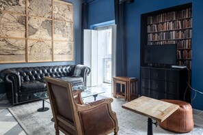 A living room with a black leather sofa, a wooden coffee table, a brown leather armchair, a glass-top table, a bookshelf, and a large world map on the wall. - Blue Home by Cadiz Time (Cádiz)
