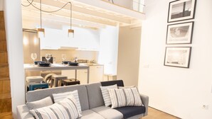 A modern living room with a grey sofa, striped cushions, a dining area with a table and chairs, and a kitchen in the background. - Casa Isabela by Cadiz Time (Cádiz)