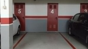 Eine Parkgarage mit nummerierten Türen, ein weißes Auto und ein schwarzes Auto sind abgestellt.