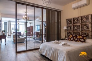 A hotel room with a large sliding glass door leading to a balcony, a bed with white linens, a decorative headboard, and a wall-mounted air conditioning unit. - La Luz de Cadiz by Cadiz Time (Cádiz)