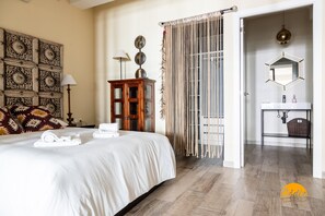 A hotel room with a neatly made bed, a wooden cabinet, a decorative wall panel, and a bathroom with a mirror and sink. - La Luz de Cadiz by Cadiz Time (Cádiz)