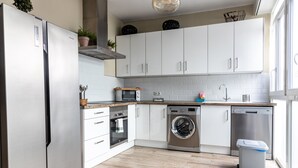 A modern kitchen with white cabinets, a stainless steel refrigerator, a built-in oven, a washing machine, and a dishwasher. - La Luz de Cadiz by Cadiz Time (Cádiz)