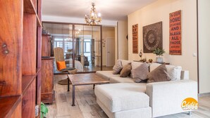 A modern living room with a sofa, coffee table, and a wooden cabinet. There is a chandelier hanging from the ceiling and a wall with decorative items. - La Luz de Cadiz by Cadiz Time (Cádiz)