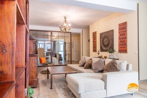 Ein modernes Wohnzimmer mit Sofa, Couchtisch und einer Holzkabine. Eine Chandelier hängt von der Decke und eine Wand ist mit Dekorationsgegenständen versehen.