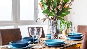 A dining table set with blue plates, clear glasses, and a vase with green leaves and flowers. - La Luz de Cadiz by Cadiz Time (Cádiz)