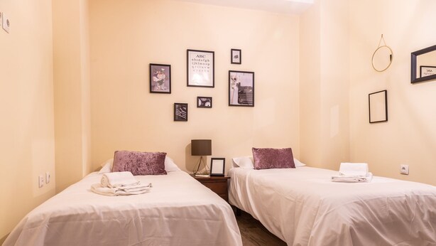 A hotel room with two beds, a nightstand, a lamp, and wall art including framed photos and a framed letter. - La Luz de Cadiz by Cadiz Time (Cádiz)