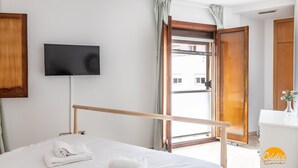 A hotel room with a bed, a TV mounted on the wall, a wooden door, and a window with curtains. - Casa Capuchinos Free Parking by Cadiz Time (Cádiz)