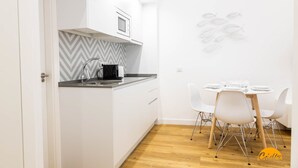 A compact kitchen with white cabinets, a black countertop, and a modern stove. There is a dining area with white chairs and a round table. - Estudio Gaviota by Cadiz Time (Cádiz)