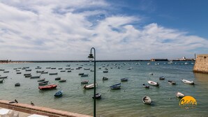 A coastal view with numerous boats docked along the shore, a stone wall, and a clear sky. - Estudio Gaviota by Cadiz Time (Cádiz)