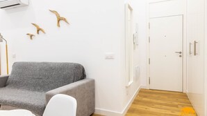 A room with a grey sofa, a white chair, a small round table, and a white door with a phone mounted on it. - Estudio Gaviota by Cadiz Time (Cádiz)