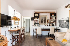 A modern living room with a wooden dining table, chairs, a sofa, a TV, a bookshelf, and a desk. - La Bella Escondida by Cadiz Time (Cádiz)