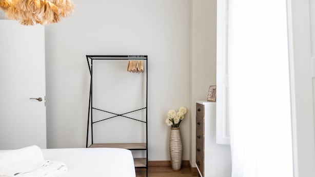 Ein Schlafzimmer mit einem Bett, einem schwarzen, metallenen Wäscheständer, einer Vase mit Blumen und einer weißen Kommode.