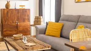 Ein Wohnzimmer mit grauem Sofa, einem Holztisch, einem Korbwäschesammler und einer Holzkommode.