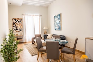 Uma sala de jantar com uma mesa posta para quatro pessoas, um sofá, uma luminária e um quadro na parede.