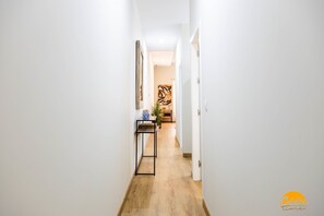 A narrow hallway with a wooden floor, white walls, and a black metal shelf with a blue object on it. - Tailor s Home by Cadiz Time (Cádiz)