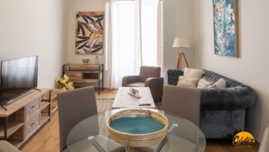 A modern living room with a flat-screen TV, a glass coffee table, a grey sofa, and a dining area with chairs. - Tailor s Home by Cadiz Time (Cádiz)
