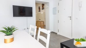 A modern hotel room with a flat-screen TV mounted on the wall, a dining area with a white table and chairs, a potted plant, and a small table with a plant on the side. - Casa Rehala Nisa by Cadiz Time (Cádiz)
