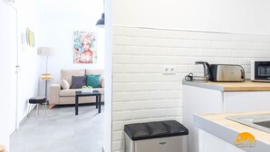 A compact living space with a kitchenette, a sofa, a small table, and a trash bin. - Casa Rehala Nisa by Cadiz Time (Cádiz)