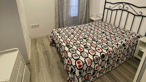 Makuuhuoneessa on kuviollinen päiväpeite, metallinen sängynpääty, yöpöytä ja pieni valkoinen kaappi.