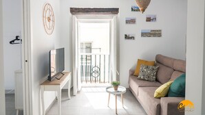 A modern living room with a TV on a wooden stand, a round coffee table with a plant, a beige sofa with patterned cushions, and a balcony with a railing. - Casa Rehala Paya by Cadiz Time (Cádiz)