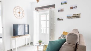 A living room with a sofa, a TV on a stand, a small table with a plant, and a door leading to another room. - Casa Rehala Paya by Cadiz Time (Cádiz)