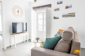 A living room with a sofa, a TV on a stand, a small table with a plant, and a door leading to another room. - Casa Rehala Paya by Cadiz Time (Cádiz)