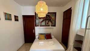 A neatly arranged bedroom with a bed, pillows, a hanging light fixture, and a window with curtains. - La Roca del Sur by Cadiz Time (Cádiz)