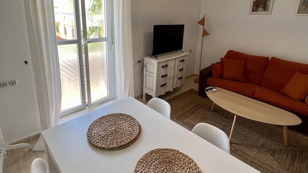 A living room with a white table, orange sofa, and a TV on a white cabinet. - La Roca del Sur by Cadiz Time (Cádiz)