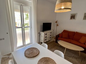 Ett vardagsrum med ett vitt bord, en orange soffa och en tv som står på ett vitt skåp.