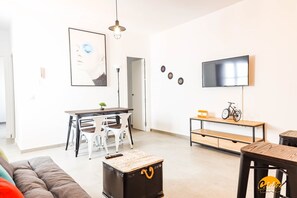 Ein modernes Wohnzimmer mit einer Couch, einem Couchtisch, einem Essbereich mit Stühlen, einem an der Wand befestigten Fernseher und einem Fahrrad auf einem Regal.