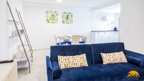 Uma sala de estar moderna com um sofá azul, uma escada e uma área de jantar ao fundo.