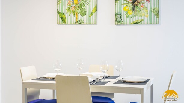 Mesa de jantar posta com pratos brancos, copos de vinho e talheres. Há duas cadeiras com almofadas azuis.