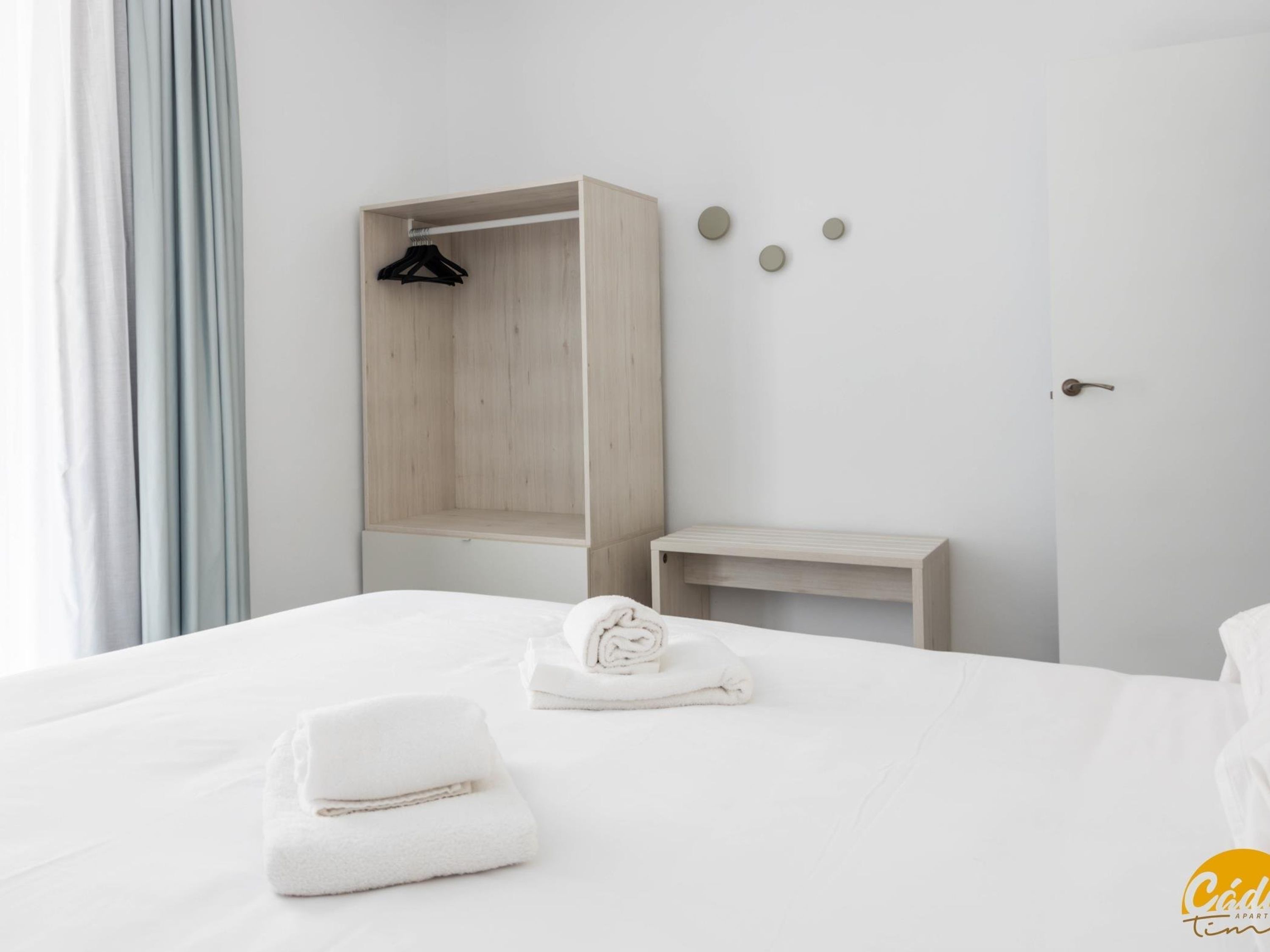 A hotel room with a bed, a wooden wardrobe, a small table, and a door.
