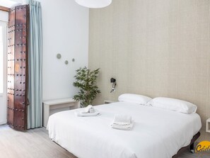 Una habitación de hotel moderna con una cama grande, una mesita de noche, una lámpara de pared y una planta en maceta.