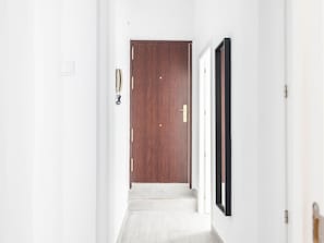 A hallway with a wooden door at the end, white walls, and a light-colored floor. - The Yellow House by Cadiz Time (Cádiz)