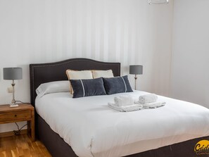 Ein ordentlich bezogenes Bett mit weißen Leinen, zwei Nachttischlampen und eine Reihe Handtücher auf dem Bett.