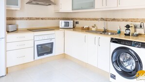 Eine moderne Küche mit weißen Schränken, einem Einbauofen, einer Mikrowelle, einem Spülbecken und einer Waschmaschine.