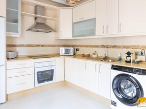 A modern kitchen with white cabinets, a built-in oven, a microwave, a sink, and a washing machine. - Balcones del Atlantico Free Parking by Cadiz Time (Cádiz)